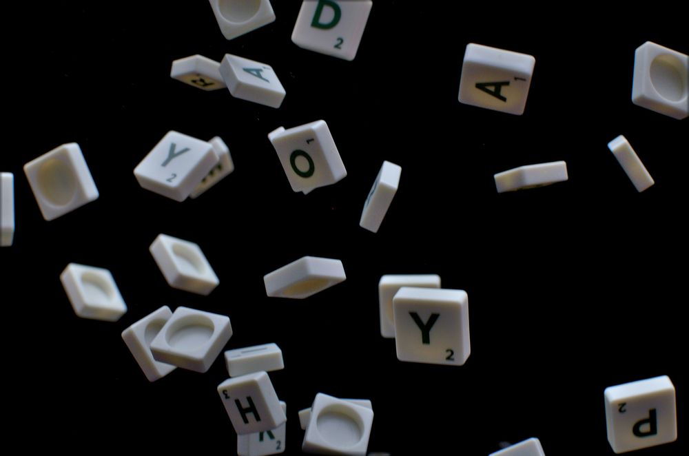 White letter tiles appear to be falling or floating against a black background, creating a scattered, chaotic effect.