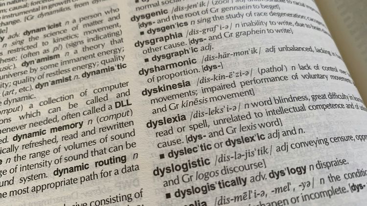 Un gros plan sur la page d'un dictionnaire ouvert. L'entrée principale visible et mise en évidence est "dyslexia" (dyslexie), avec sa définition : "a word blindness, great difficulty in learning to read or spell, unrelated to intellectual competence and of unknown cause."