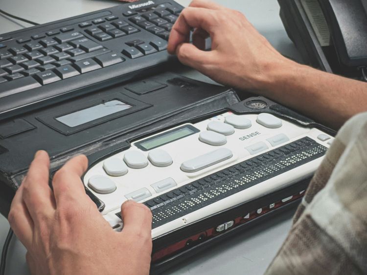 Main utilisant un afficheur braille électronique posé devant un clavier d’ordinateur.